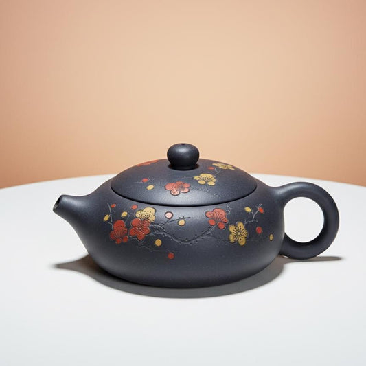 Black ceramic teapot with floral designs on a white surface and beige background